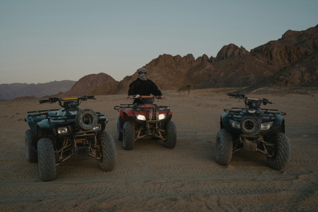 A person sits on an ATV in a rugged desert surrounded by mountains.